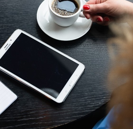 bord med en kaffekopp och en telefon samt en kvinna i förgrunden som syns uppifrån