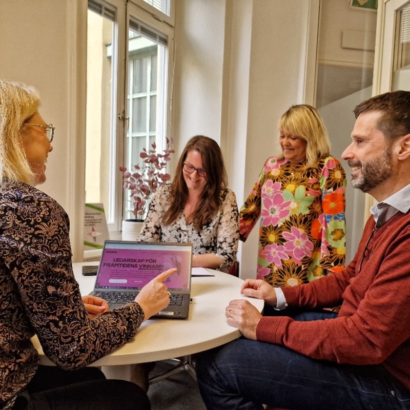 Fyra personer sitter tunt ett bord i ett möte, på bordet står en laptop med en hemsida med texten Ledarskap för framtiden vinnare